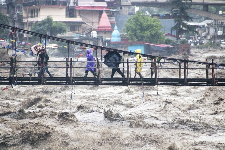 People walk through a bridge across River Beas swollen due to heavy rains in Kullu District, Himachal Pradesh, India, Monday, July 10, 2023. Scientists have long warned that more extreme rainfall is expected in a warming world. 