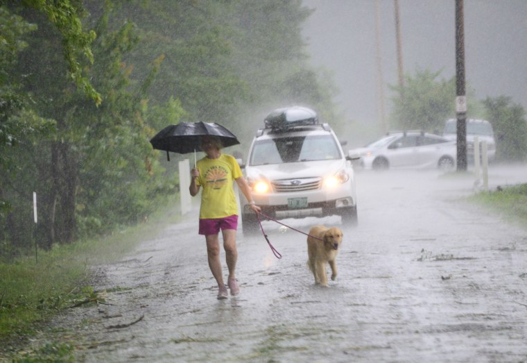 Nancy Cain walks her dog as the rain pours down near the West River in Brattleboro, Vt., on July 10, 2023. 