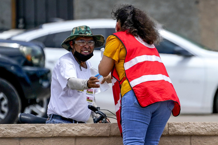 Image: Salvation Army volunteer Soila Arias gives water to a man at their Valley Heat Relief Station on July 11, 2023 in Phoenix. 