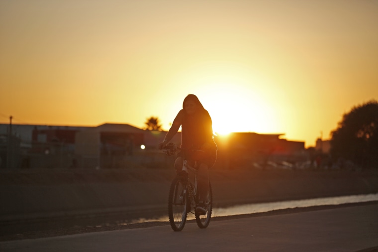 A woman rides her bicycle next to the Grand Canal as a very hot day ends in Phoenix on July 6, 2023. 