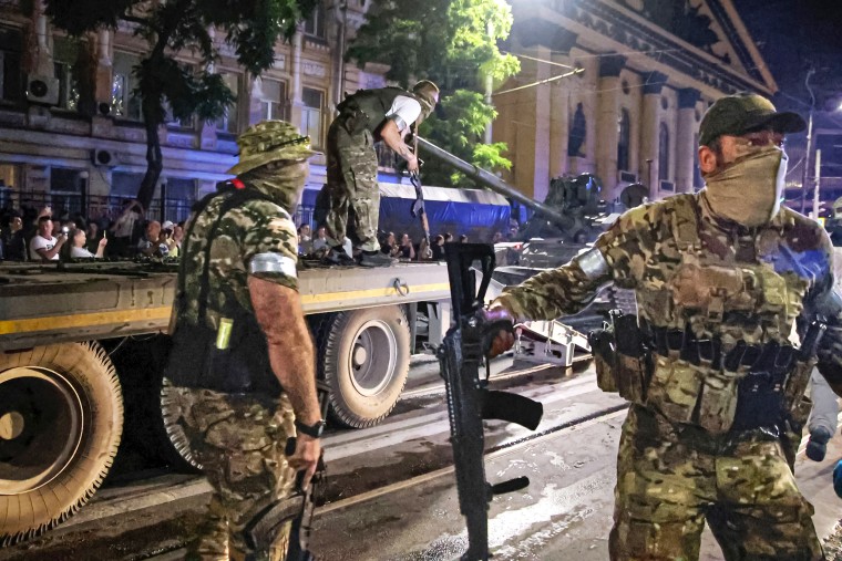 FILE - Members of the Wagner Group military company guard an area as other load their tank onto a truck on a street in Rostov-on-Don, Russia, Saturday, June 24, 2023, prior to leaving an area at the headquarters of the Southern Military District. Russia's rebellious mercenary chief Yevgeny Prigozhin walked free from prosecution for his June 24 armed mutiny. In the meantime, a campaign appears to be underway to portray the founder of the Wagner Group military contractor as driven by greed.