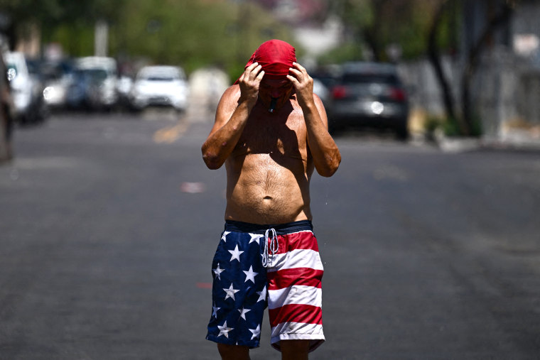 Water drips from a person as they grasp at their head covering during a record heat wave in Phoenix