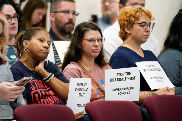 Women hold signs opposing charter schools linked to Hillsdale College during a meeting of the Tennessee Public Charter School Commission staff in Murfreesboro, Tenn., on Sept. 14, 2022.