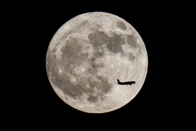 An airplane flies past a super full moon called a Buck moon over Los Angeles in July 2023.