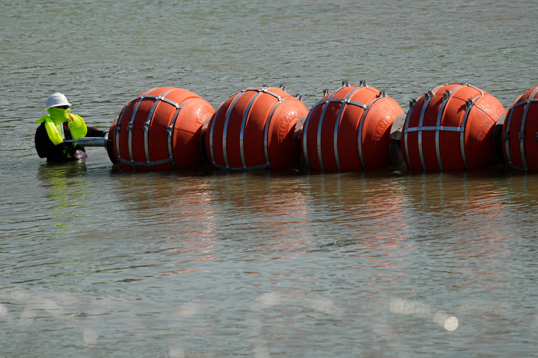 A worker helps deploy a string of large buoys to be used as a border barrier at the center of the Rio Grande near Eagle Pass, Texas, on July 11, 2023. 