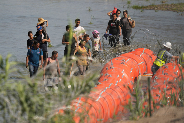 Los migrantes que intentan ingresar a los Estados Unidos desde México se acercan al sitio donde los trabajadores ensamblan grandes boyas para usarlas como barrera fronteriza a lo largo de las orillas del Río Grande en Eagle Pass, Texas, el 11 de julio de 2023.