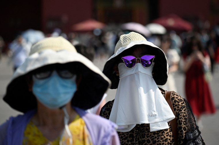 A woman shelters under a mask as she walks out of the Forbidden City during hot weather conditions in Beijing