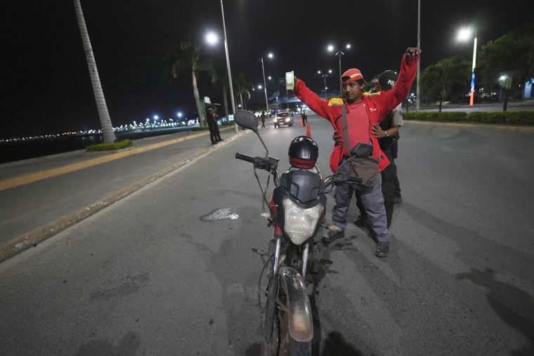 Police frisk a motorcycle driver for weapons during a curfew in Manta, Ecuador