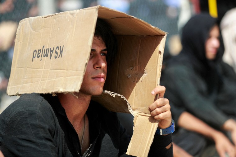 A man shields himself from the sun with a cardboard box during an Ashura event in Baghdad on July 29, 2023.