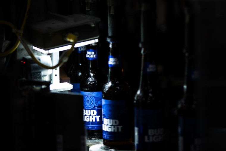 A machine seals glass bottles of Bud Light brand beer with caps.