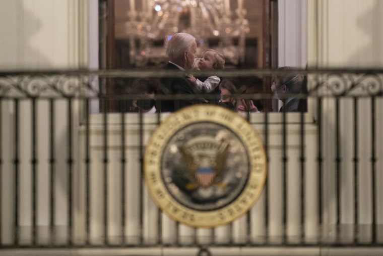 Joe Biden holds a young boy in his arms, as seen through a window of the white house.