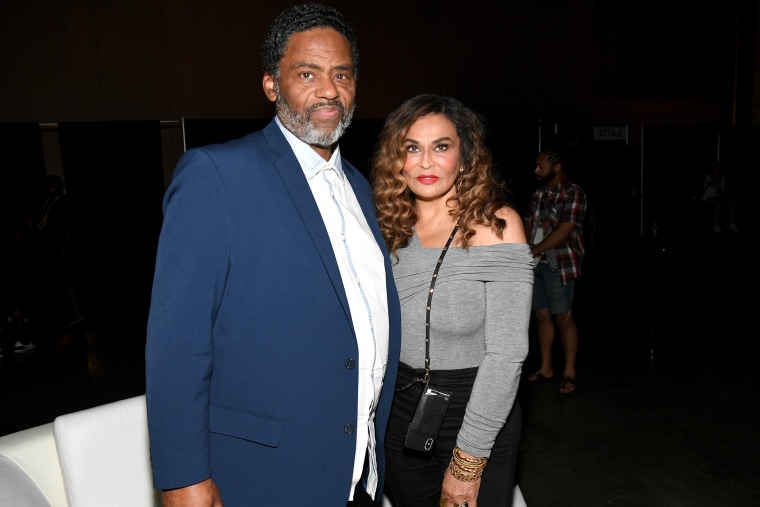 Richard Lawson in a blue suit and Tina Knowles Lawson in a grey shirt and black pants pose for a photo.
