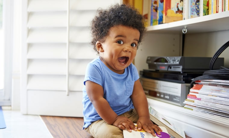 Surprised Black baby boy sitting on floor playing with books