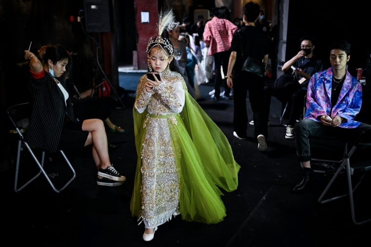 A young model looks at her mobile phone as she waits backstage during the China Fashion Week in Beijing on September 3, 2021.