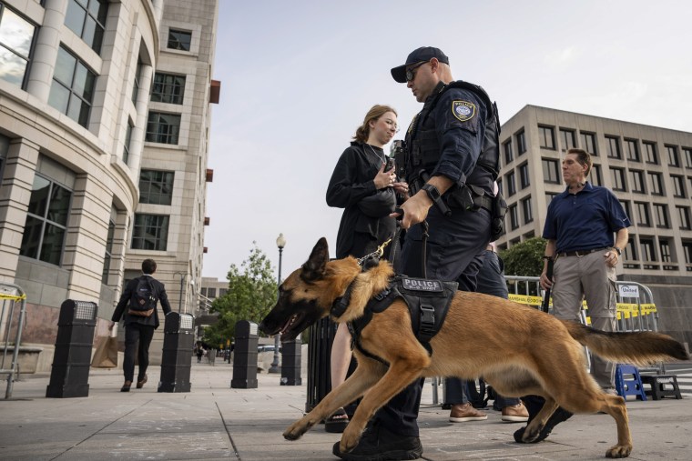 A police officer and a dog patrol the perimeter of the E. Barrett Prettyman Courthouse