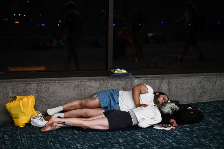 Image: Passengers sleep on the floor of Kahului Airport on Tuesday. Flights were cancelled and delayed, leaving people stranded in Maui as fires raged.