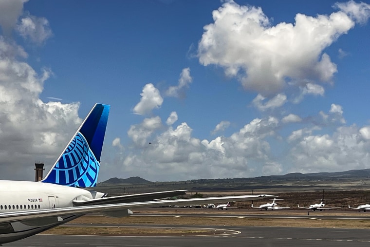 The United Airlines plane leaving Maui, with a helicopter carrying in a water buffalo behind, on Aug. 9, 2023.