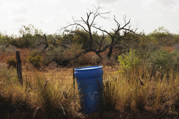 A water station for immigrants sits along a fence line near a roadway in Jim Hogg County, Texas