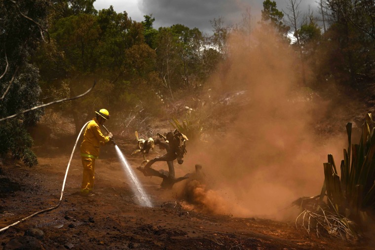 A Maui County firefighter extinguishes a fire near homes in Kula, Hawaii
