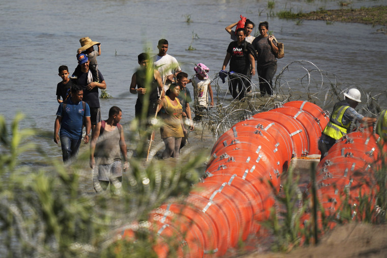 Migrants approach the site where workers are assembling large buoys in the Rio Grande