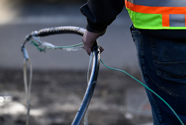 A telecommunications construction company worker gets ready to feed a cable underground during broadband installation in Boulder, Colo., as part of the city's gigabit speed broadband buildout in 2022.