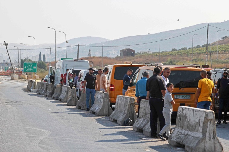 People wait after Israeli security forces closed a road following a reported attack in Huwara