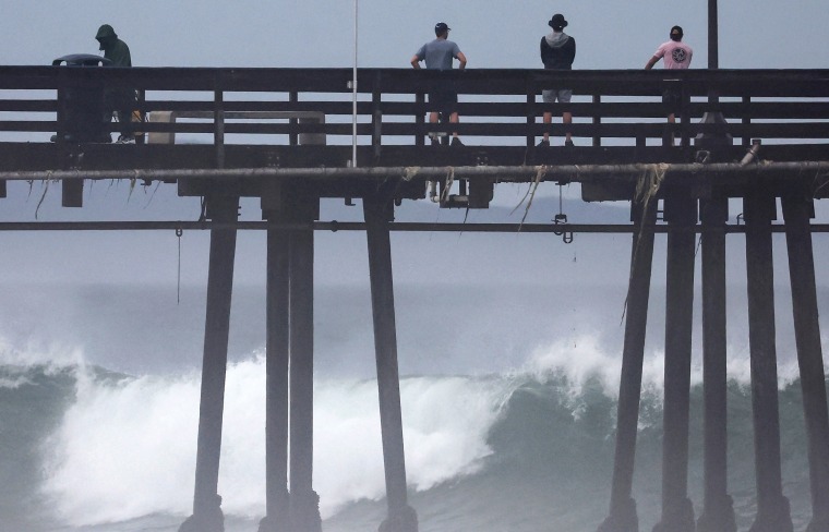 People stand on a pier over the Pacific Ocean as Hurricane Hilary approaches in Imperial Beach, Calif., on Aug. 20, 2023.
