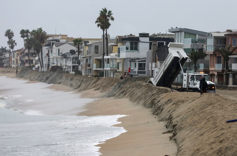 Workers build a sand berm outside of beachfront homes in Long Beach, Calif., on Aug. 20, 2023.