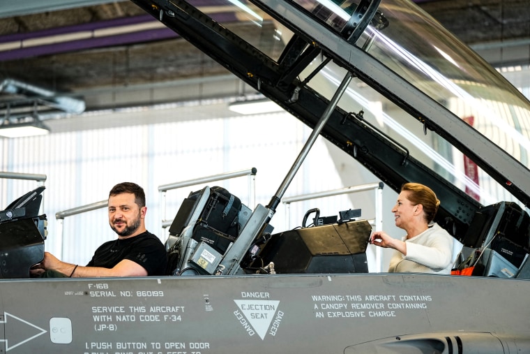 Ukrainian President Volodymyr Zelensky and Danish Prime Minister Mette Frederiksen react as they sit in a F-16 fighter jet in the hangar of the Skrydstrup Airbase in Vojens, northern Denmark, on Aug. 20, 2023.