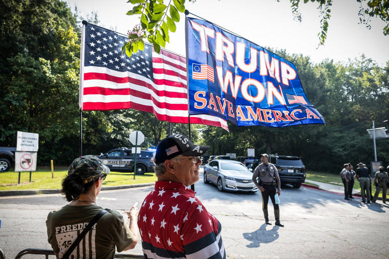 Image: Supporters of former President Donald Trump, Georgina and Cliff MacMorris hold flags outside of the Fulton County Jail ahead of Trump's surrender on Aug. 24, 2023 in Atlanta.