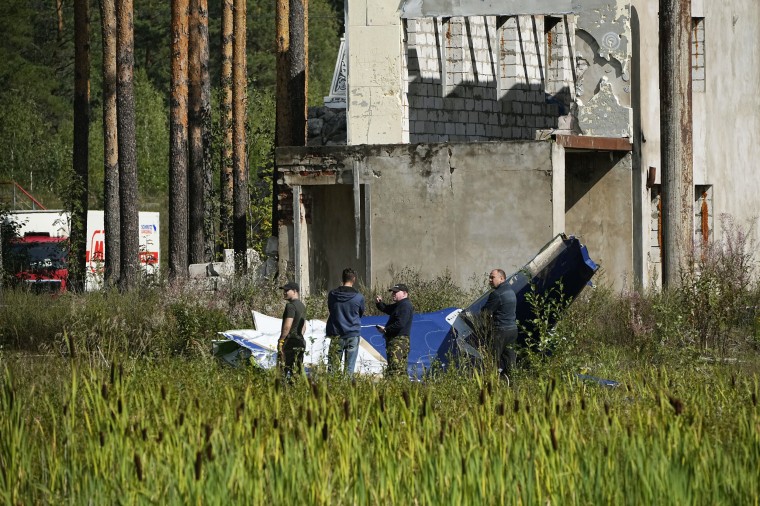 Russian servicemen inspect a part of a crashed private jet near the village of Kuzhenkino, Russia