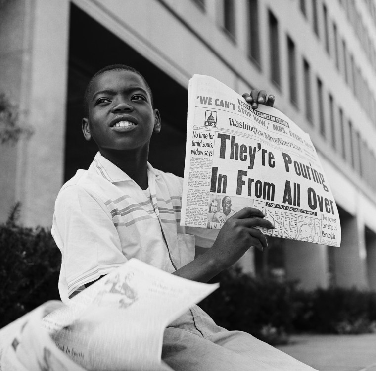 A young paperboy holds up a newspaper with the headline "They're Pouring In From All Over."