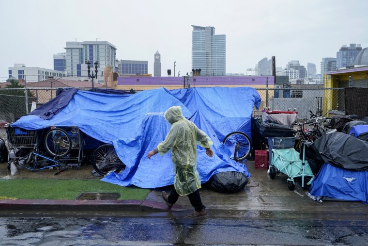 Un hombre sin casa usa coberturas de plástico para protegerse de la lluvia en el centro de San Diego, el domingo 20 de agosto de 2023.

