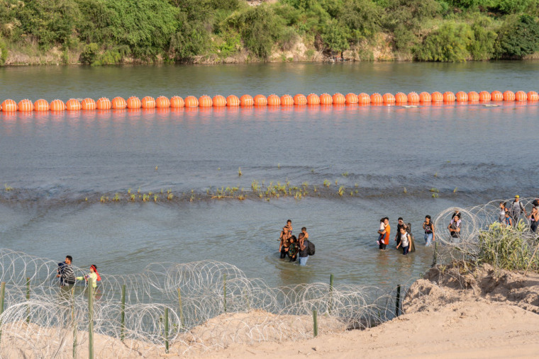 Migrantes caminan a lo largo de las boyas colocadas en el río Grande, en Eagle Pass, Texas, en la frontera con México, el 16 de julio de 2023.
