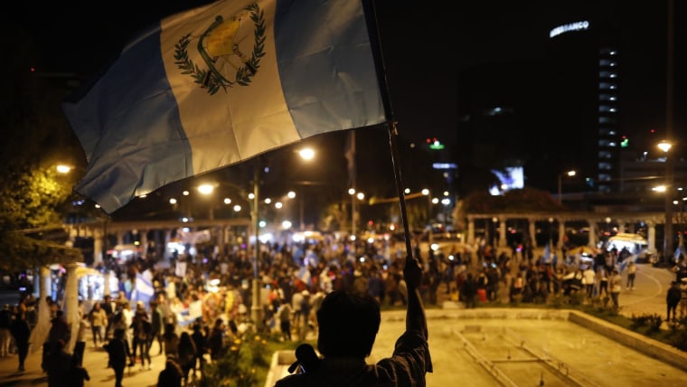 Un hombre ondea una bandera guatemalteca frente a cientos de personas congregadas en una plaza de Ciudad de Guatemala después de que cerraron las casillas para votar en la segunda vuelta presidencial de agosto de 2023
