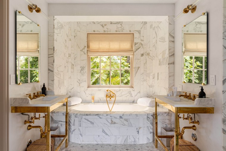 A white and gray marble tub is flanked by two marble sings with exposed gold piping.