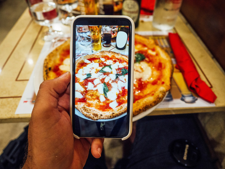 A man is taking a photo of his pizza in a restaurant.