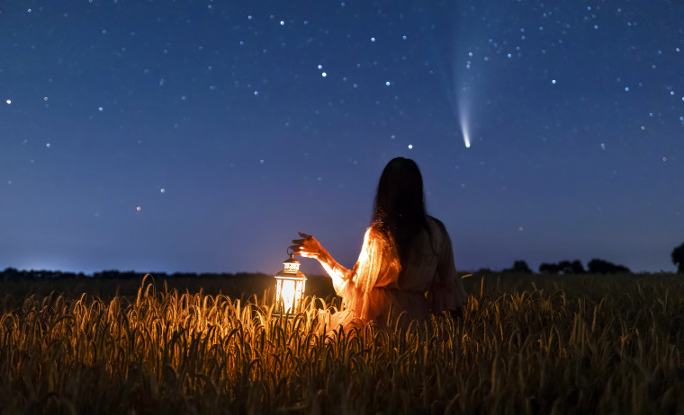 Woman in field at night with lantern.