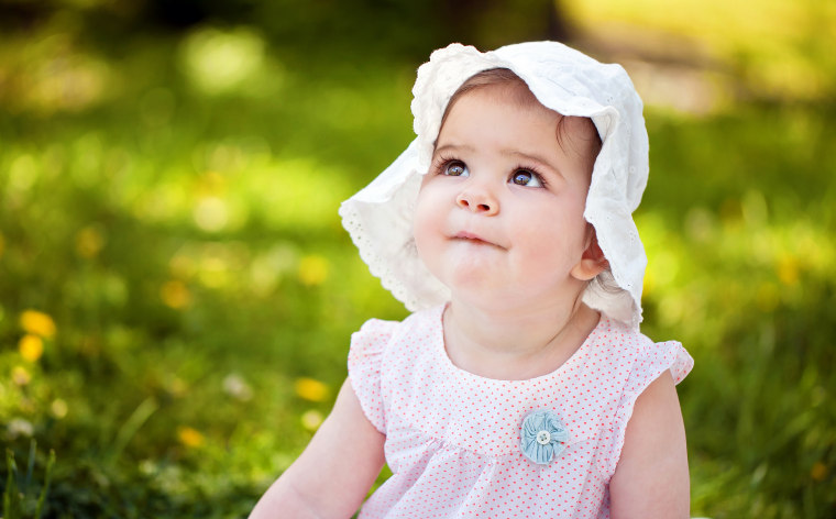 Cute baby girl with hat sitting on the grass.