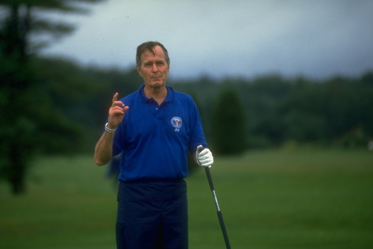 Then-President George H.W. Bush speaks to the press while golfing