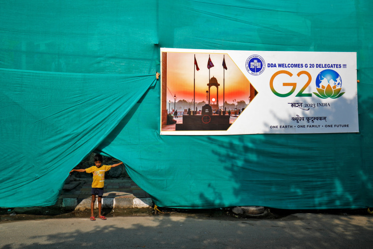 A boy pulls up plastic sheeting placed to screen a slum area alongside a road ahead of G20 Summit in New Delhi