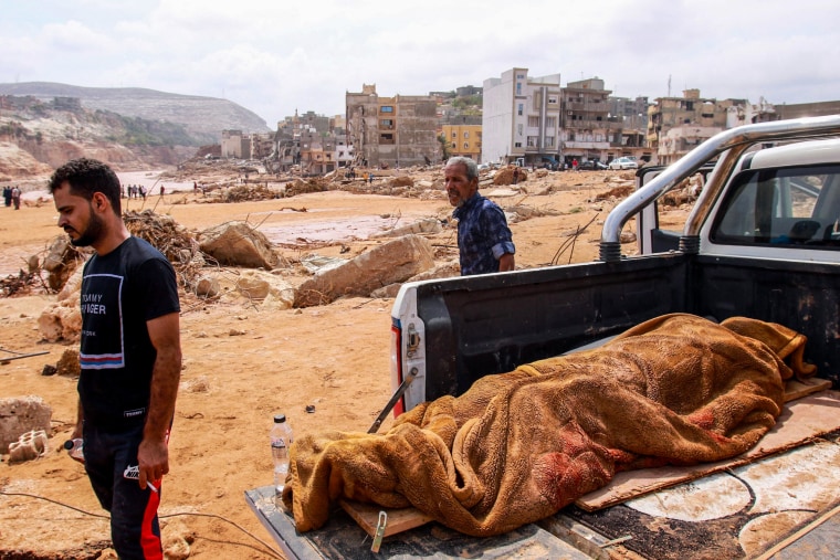 People walk past the body of a flood victim in Derna, Libya, on Sept. 11, 2023.