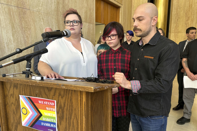 Parents Devon and Robert Dolney, of Fargo, stand with their 12-year-old child, Tate, center, during a press conference,  Thursday, Sept. 14, 2023,, at the state Capitol in Bismarck, N.D. Tate Dolney is a transgender boy and a plaintiff in a lawsuit to block North Dakota's ban on gender-affirming care for minors. The law passed North Dakota's Republican-controlled Legislature overwhelmingly earlier this year. Republican Gov. Doug Burgum signed the bill into law in April. A Gender Justice sign on the press conference lectern reads "We stand with North Dakota families." (AP Photo/Jack Dura)