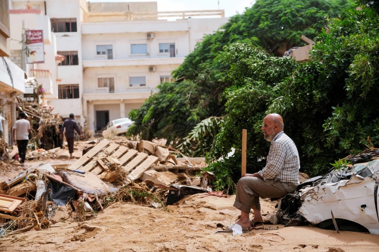 A man sits on a damaged car, after a powerful storm and heavy rainfall hit Libya, in Derna