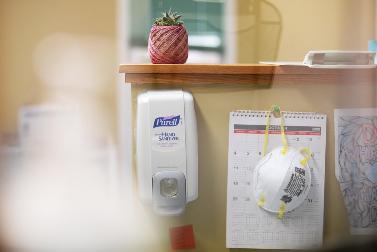 An N95 protective mask hangs next to a hand sanitizer dispenser on a reception's desk at a clinic