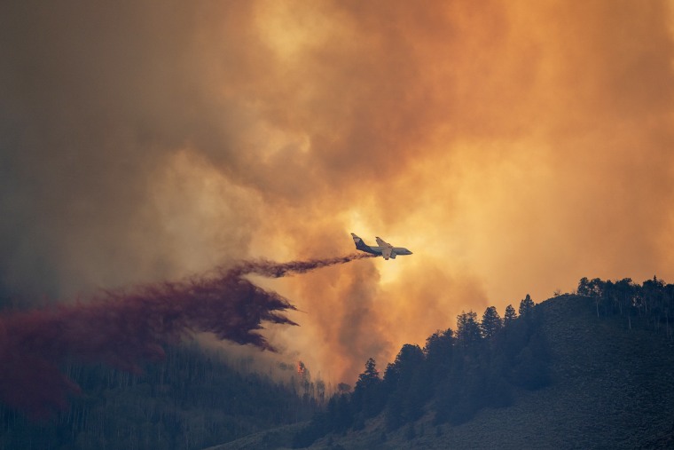 GUNNISON, COLORADO - JULY 26: A plane drops retardant as smoke billows and flames rise from the Lowline fire on July 26, 2023 near Gunnison, Colorado. The US Forest Service said the fire was started by lightning and has forced evacuations in the area.