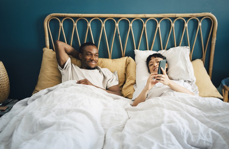 Smiling girlfriend sharing smart phone with boyfriend while lying on bed