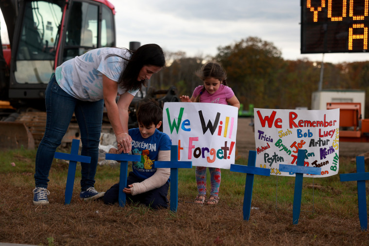 Bre Allard and her children Zeke Allard, 8, and Lucy Allard, 5, place crosses and signs in the ground near the Schemengees Bar on Oct. 28, 2023 in Lewiston, Maine. 
