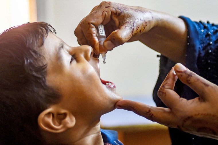 A child holds their mouth open to receive drops of polio vaccine from a vial