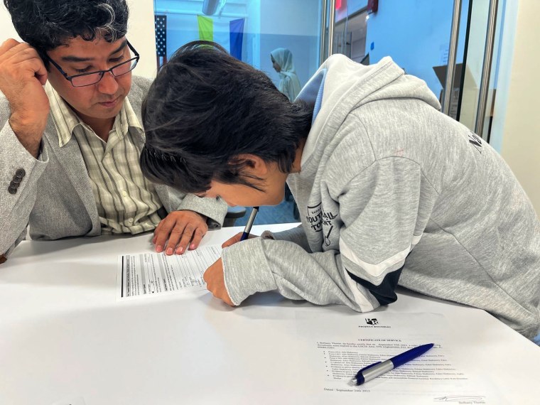 Atta looks on as his son Edris signs his own TPS application.